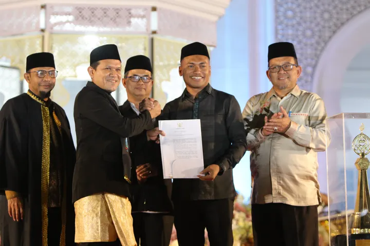 Wakil Gubernur Aceh Fadhlullah menyerahkan Surat Keputusan Gubernur tentang penetapan tuan rumah MTQ Aceh ke-38 kepada Bupati Aceh Barat Daya, Dr. Safaruddin, pada malam penutupan MTQ ke-37 di Pidie Jaya, Jumat (7/11/2025).